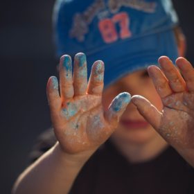 Child showing glitter and paint on hands representative of germs and hand washing necessity.