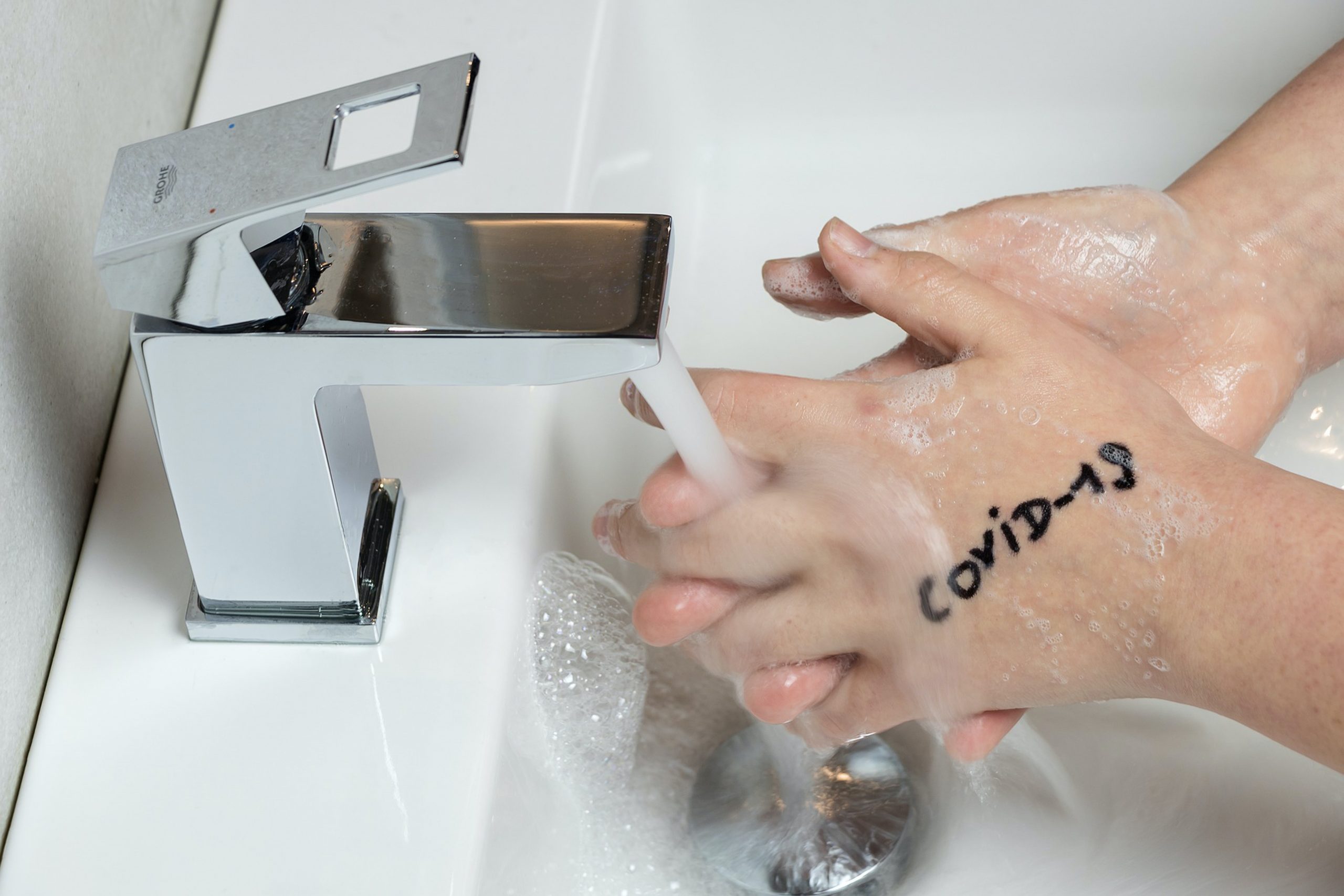 Someone washing hands with COVID-19 written in marker on top hand demonstrating how COVID hand washing has emerged.